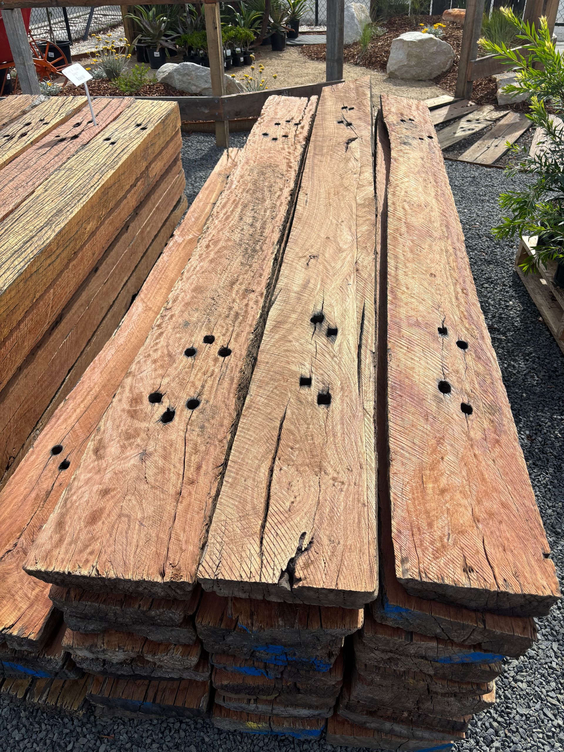 Pile of weathered, brown wooden planks with holes, stacked outdoors  — Schutz Landscape and Garden Supplies in Tomerong, NSW