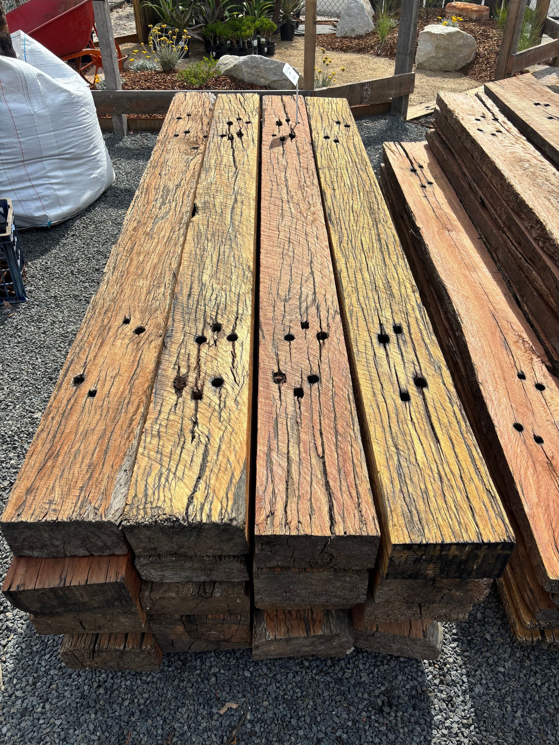 Stack of weathered, rectangular wood beams. Several display bolt holes and varying shades of brown  — Schutz Landscape and Garden Supplies in Tomerong, NSW