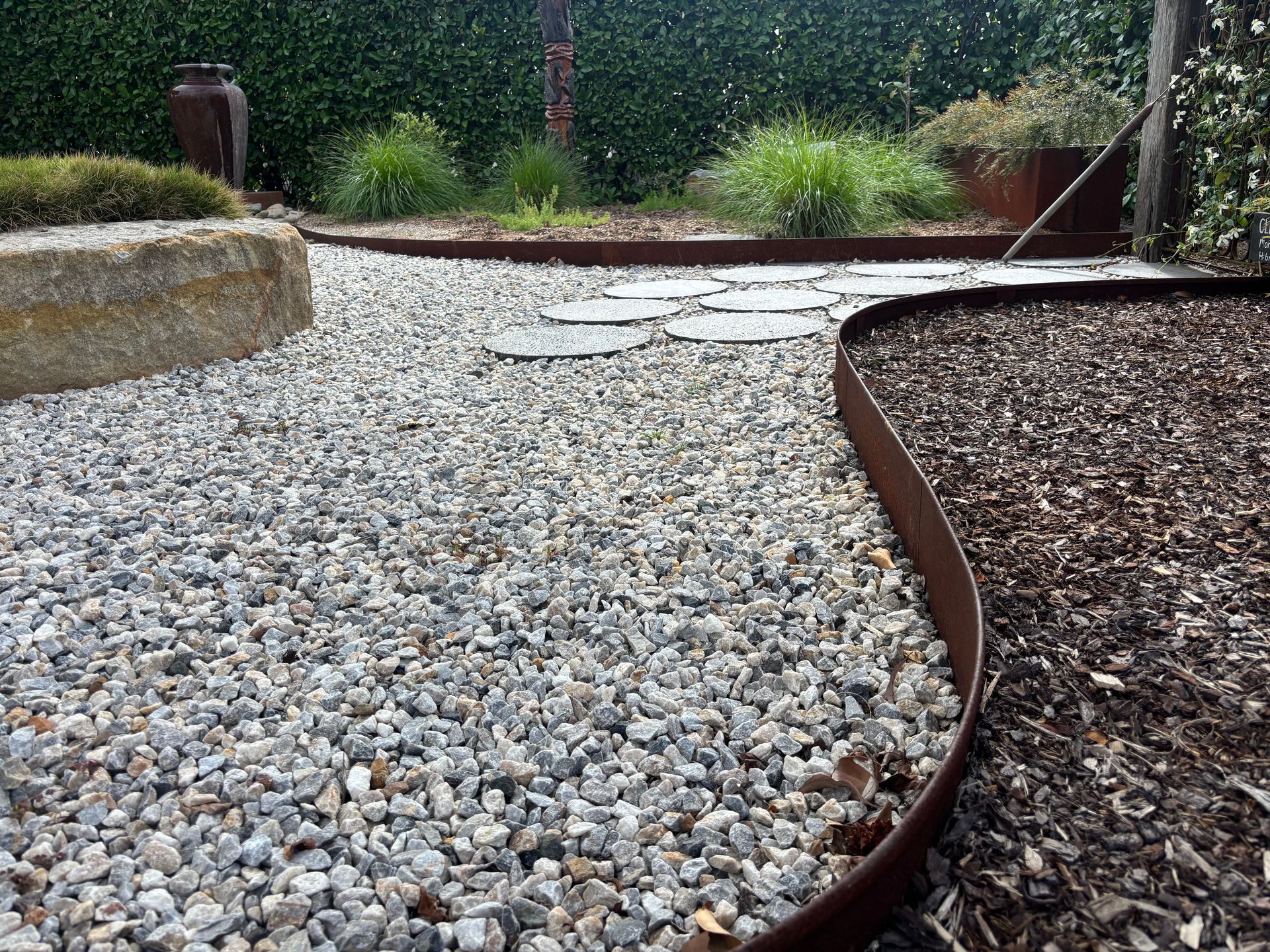 Gravel and mulch pathways separated by a metal border in a garden, with plants and greenery in the background — Schutz Landscape and Garden Supplies in Tomerong, NSW