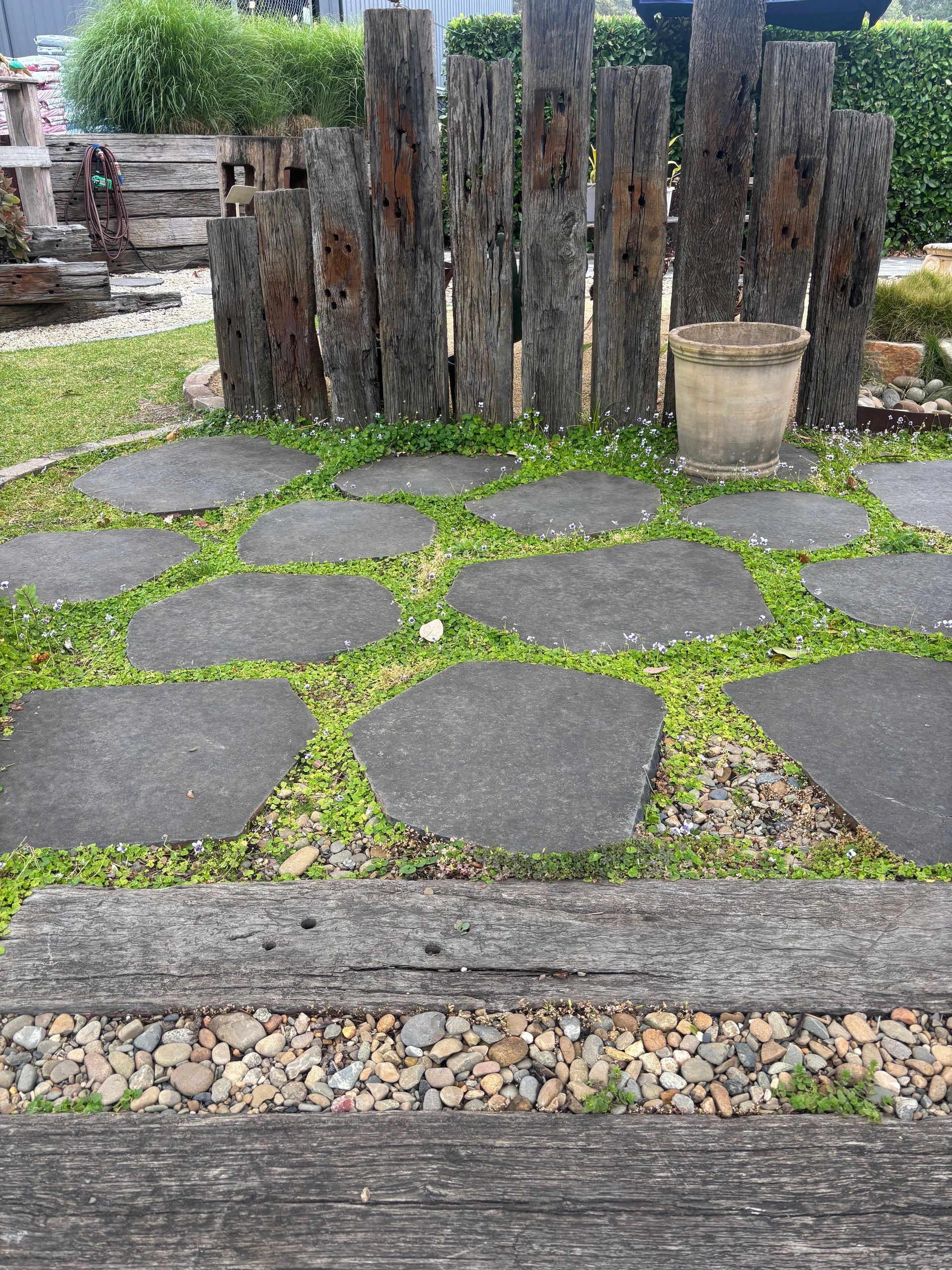 Stone path through grass with wooden posts and a pot in a garden setting  — Schutz Landscape and Garden Supplies in Tomerong, NSW