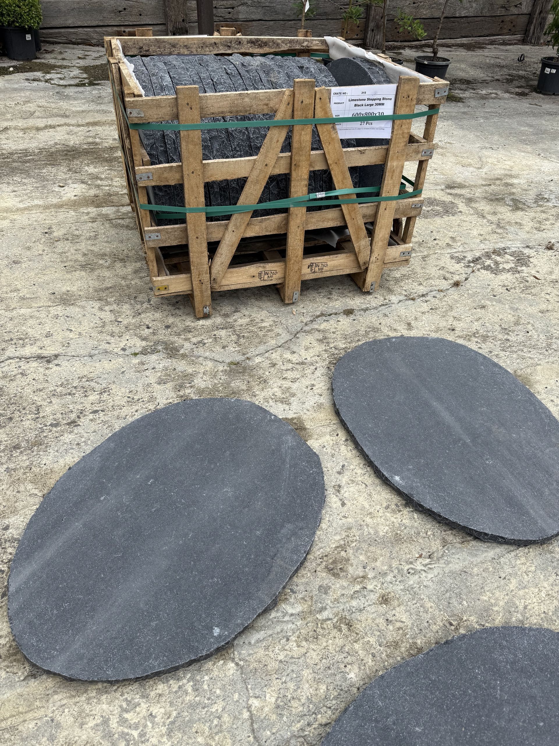 Wooden crate of dark stone tiles, with several oval-shaped tiles in front, on a concrete surface  — Schutz Landscape and Garden Supplies in Tomerong, NSW