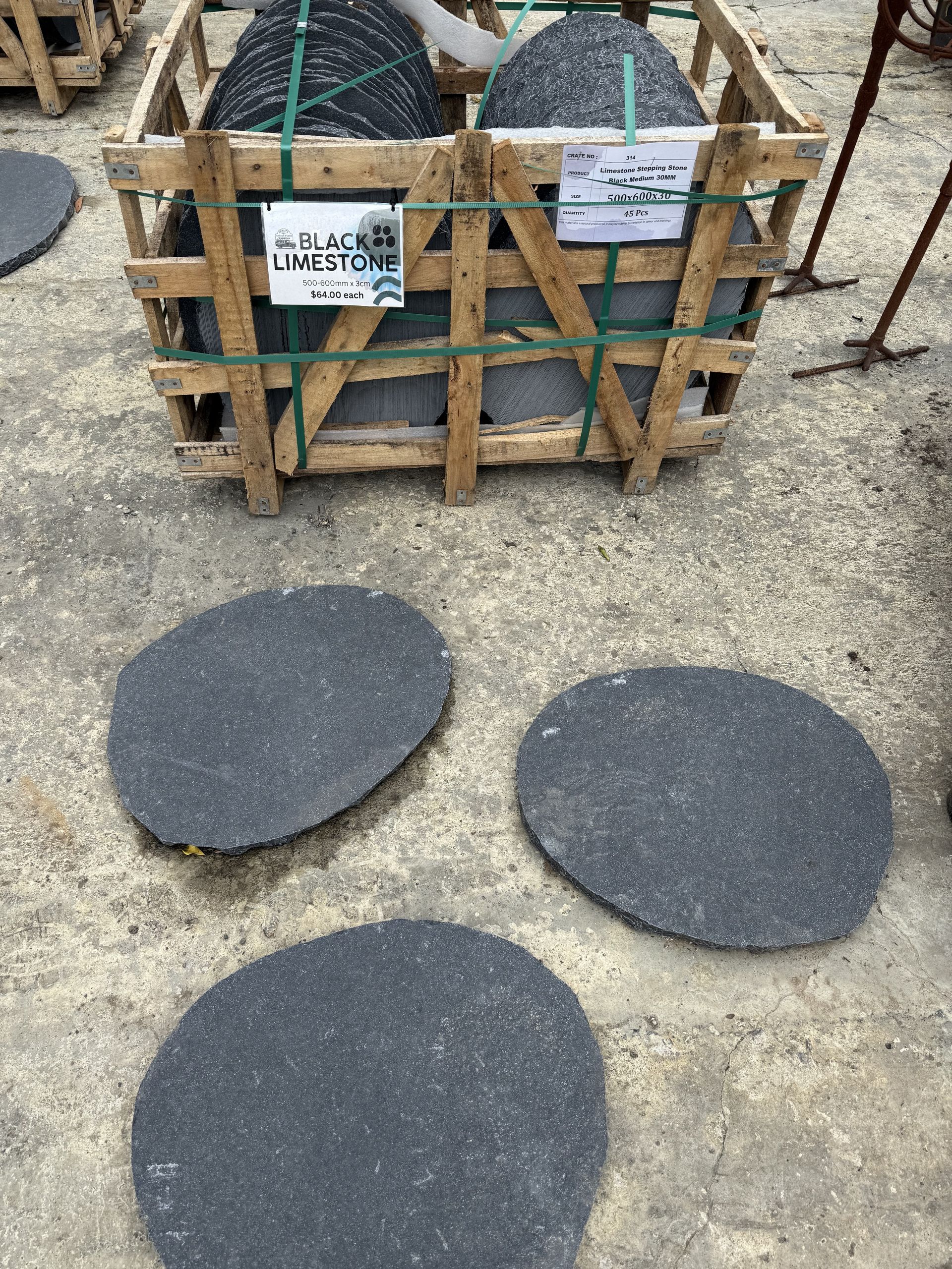 Wooden crate holding black stone pavers, three loose pavers in front on a concrete surface  — Schutz Landscape and Garden Supplies in Tomerong, NSW