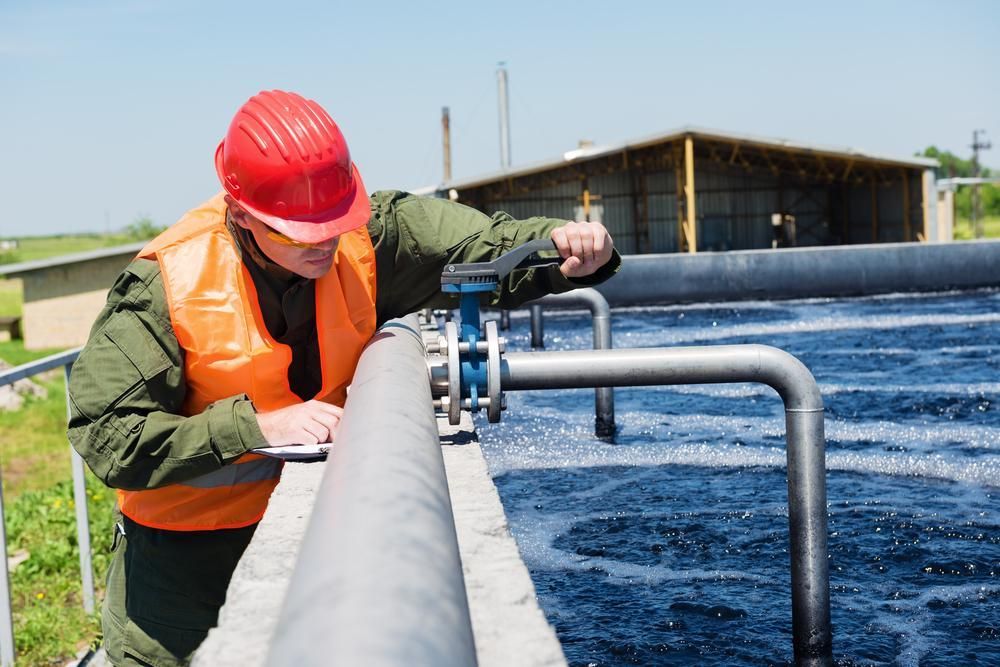 A Man Wearing A Hard Hat And Orange Vest Is Working On A Pipe — Gympie Septic Pump Outs In Poona, QLD
