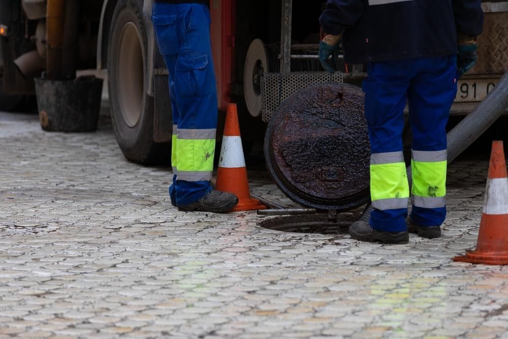 Two Men Are Working On A Manhole Cover On A Cobblestone Street — Gympie Septic Pump Outs In Banks Pocket, QLD