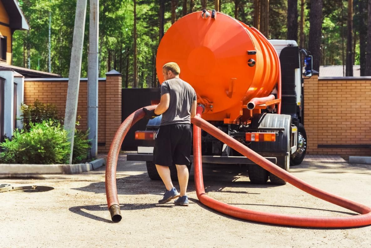 A Man Is Standing Next To A Vacuum Truck With A Hose Attached To It — Gympie Septic Pump Outs In Rainbow Beach, QLD