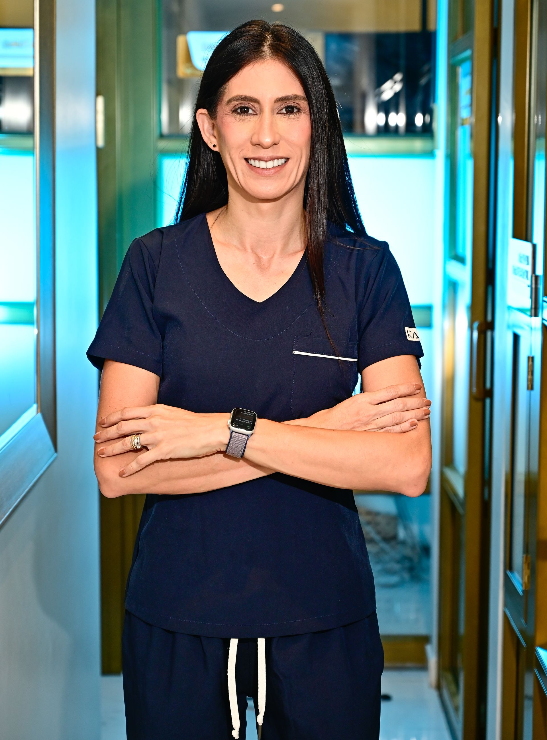 Una mujer con una blusa azul está parada en un consultorio dental con las manos juntas.