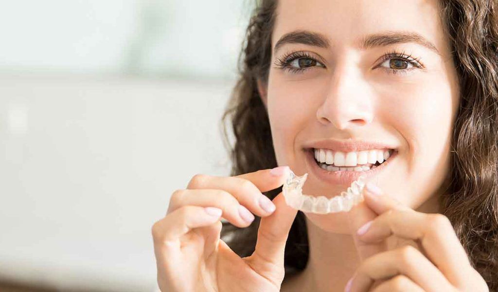Una mujer sostiene un aparato transparente delante de sus dientes.
