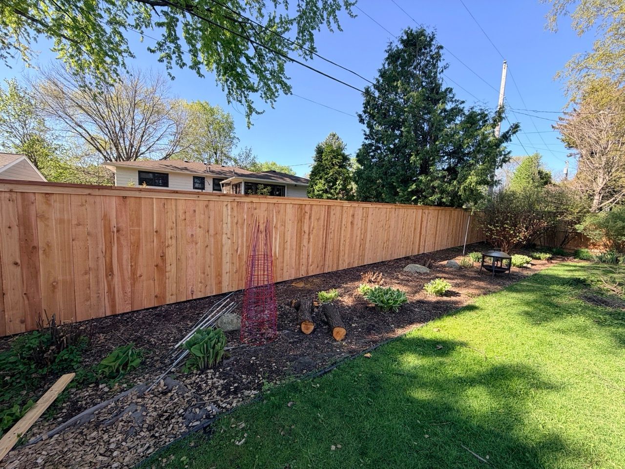 Wooden backyard fence beside a mulched garden bed and green lawn under a clear blue sky