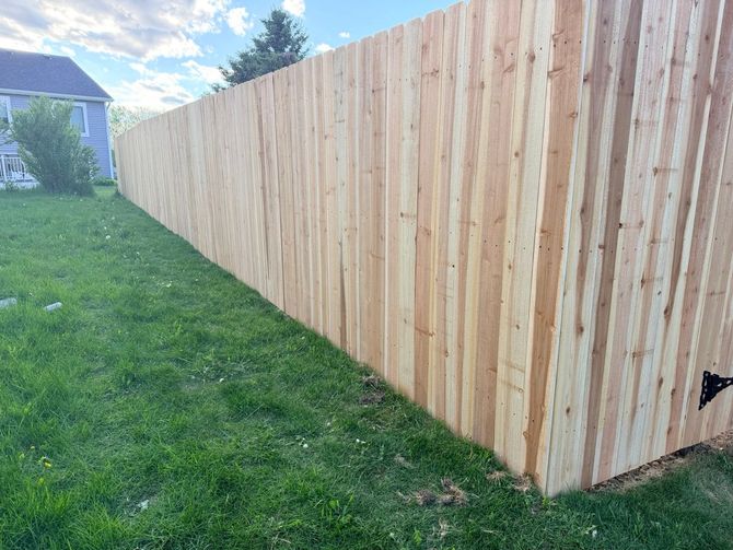 Long wooden privacy fence beside a grassy yard under a partly cloudy sky