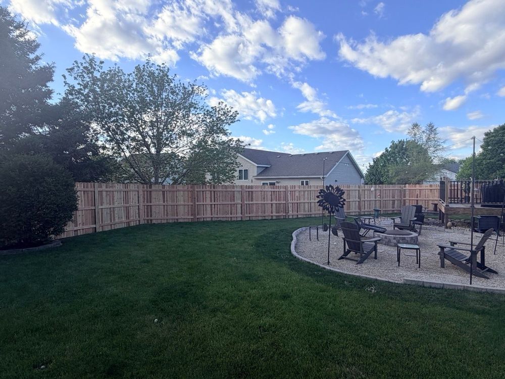 Backyard with green lawn, wooden fence, patio seating, and partly cloudy sky