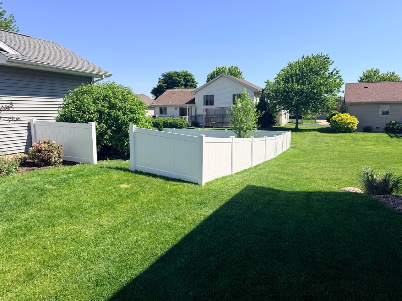Suburban backyard with green lawn, white fence, and houses under a clear blue sky