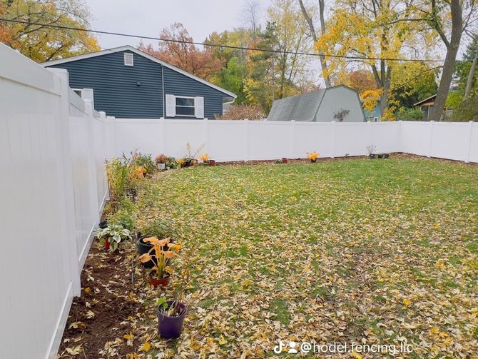 Fenced backyard with green lawn, fallen leaves, and a white privacy fence around the yard