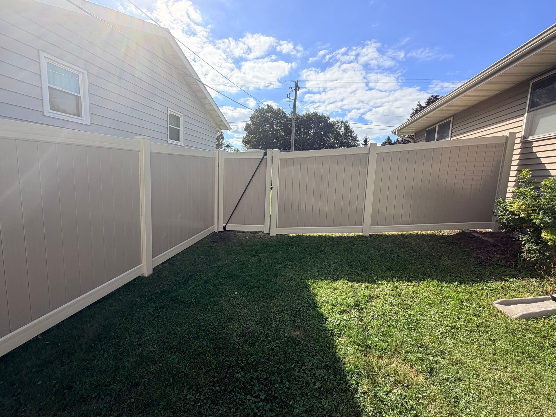 Backyard with green grass, white vinyl fences, and a partly cloudy blue sky.