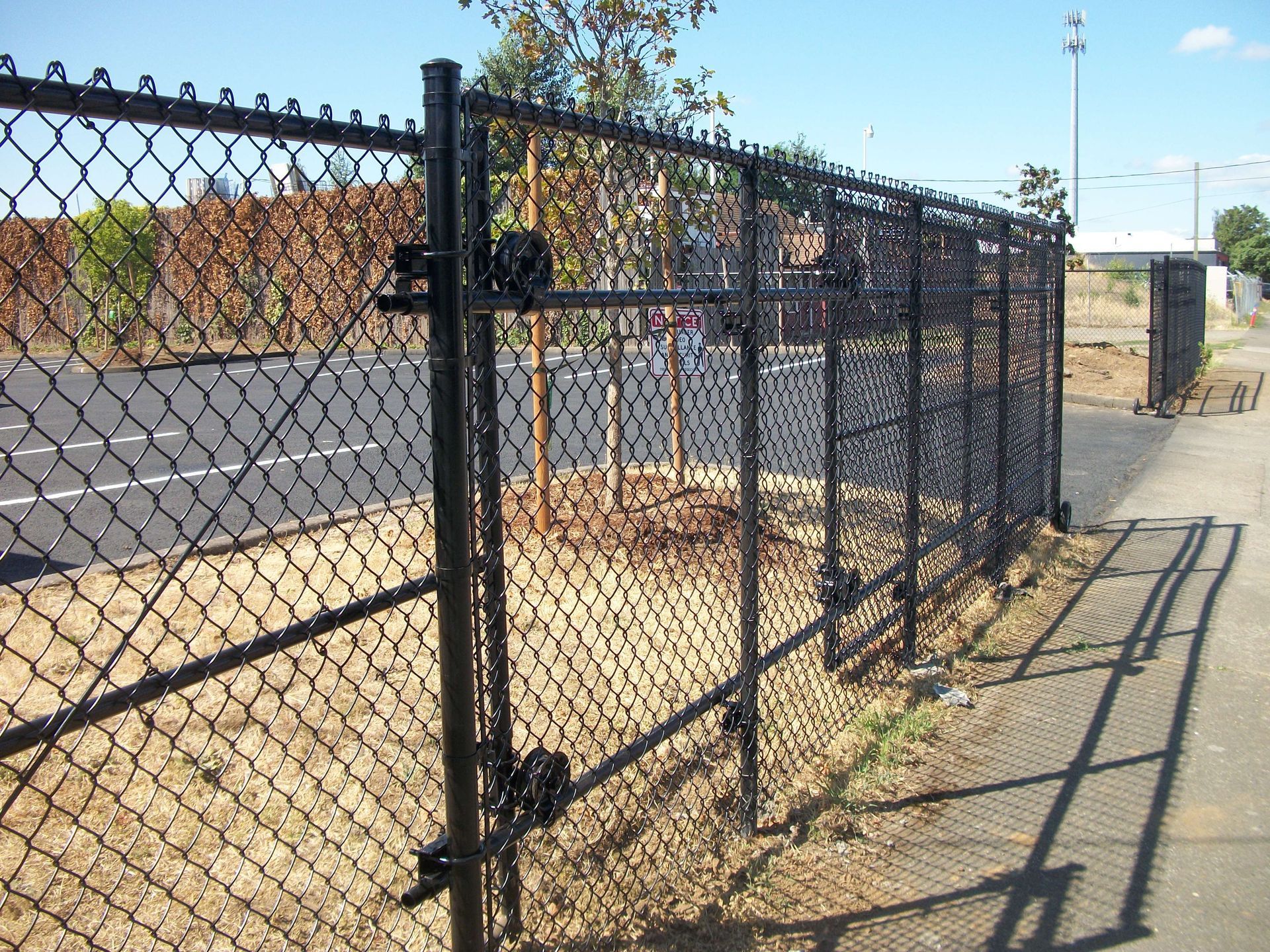 Chain-link fence beside a sidewalk and empty lot, casting long shadows in bright sunlight.