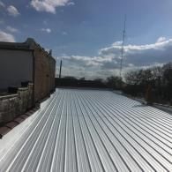 A freshly installed white, corrugated metal roof under a bright blue sky with scattered clouds.
