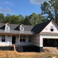 A newly constructed house with a gray roof, metal porch accents, and white exterior sheathing under a blue sky.