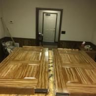 Two large wooden doors with a striped grain finish lie flat in a room, with an open doorway visible in the background.