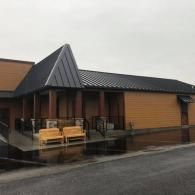 Tan-colored building with a dark metal roof, featuring a covered patio with two wooden benches on a rainy day.