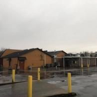 A side view of a brick commercial building on a wet, overcast day with yellow bollards in the foreground.