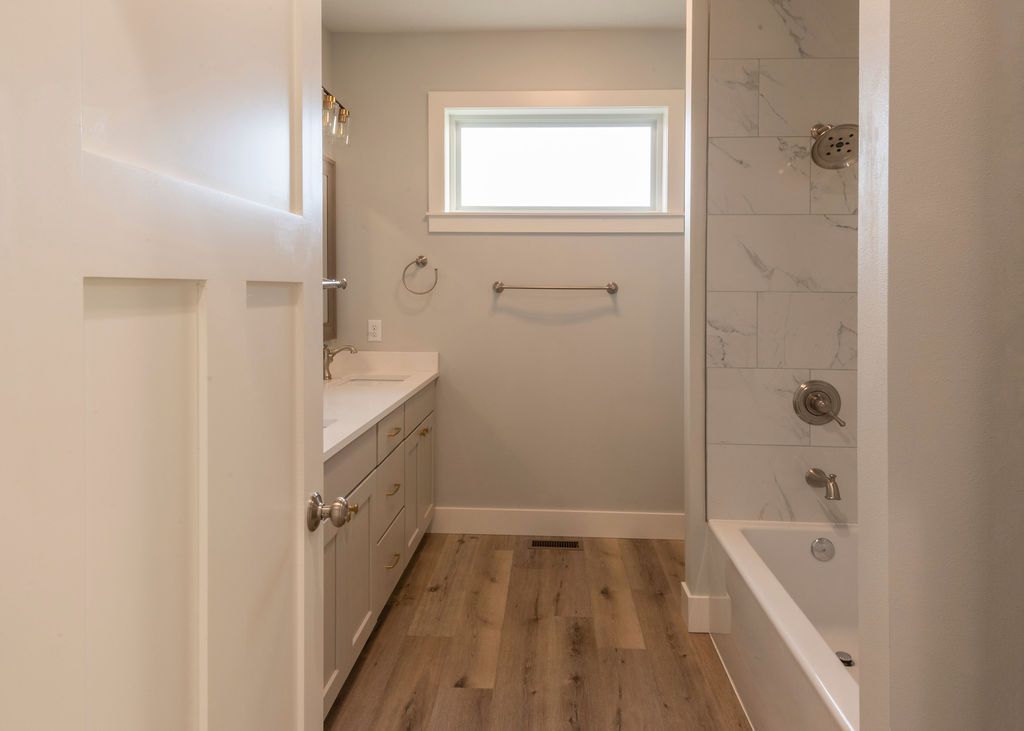 Bathroom with light wood floor, white vanity, tub, and a small window.