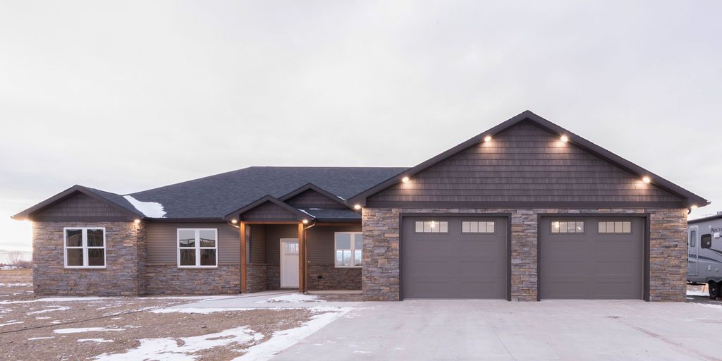 Brick house with a two-car garage. Driveway and yard covered in snow. Overcast sky.