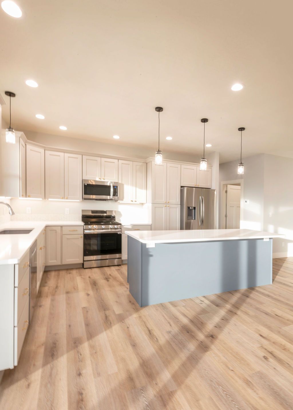 Modern kitchen with white cabinets, blue island, stainless steel appliances, and hardwood floors.