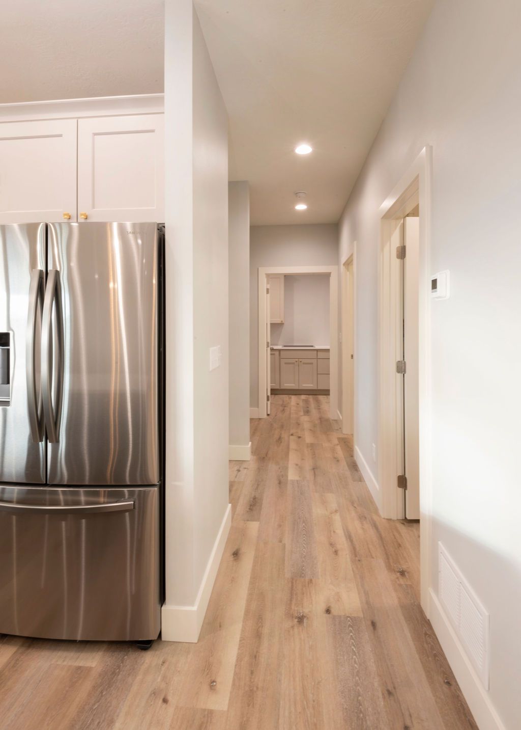 Stainless steel refrigerator beside hallway with light wood flooring and gray walls.