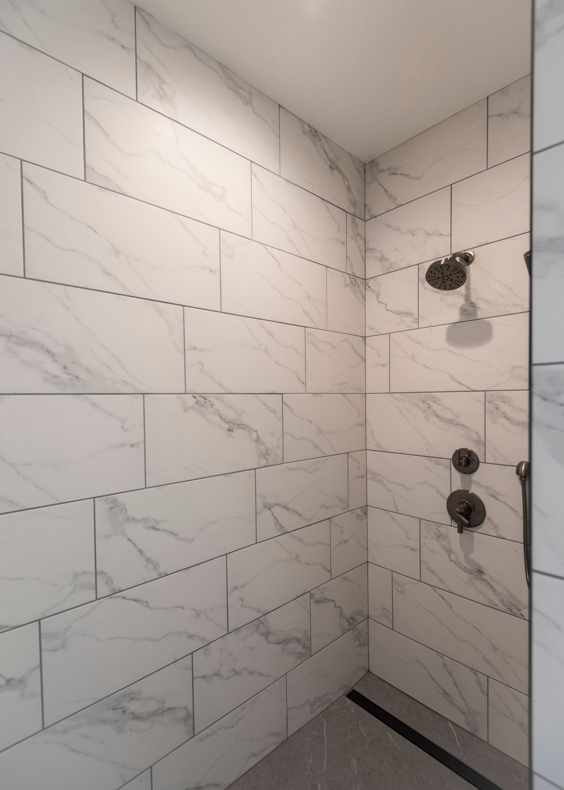 Tiled shower with marble-like patterns, featuring a rainfall showerhead and bronze fixtures.