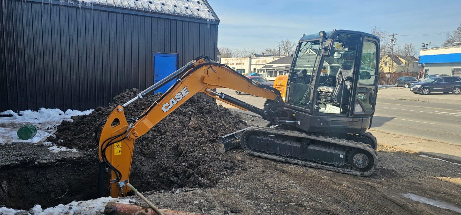 A small excavator is digging a hole in the ground in front of a building.