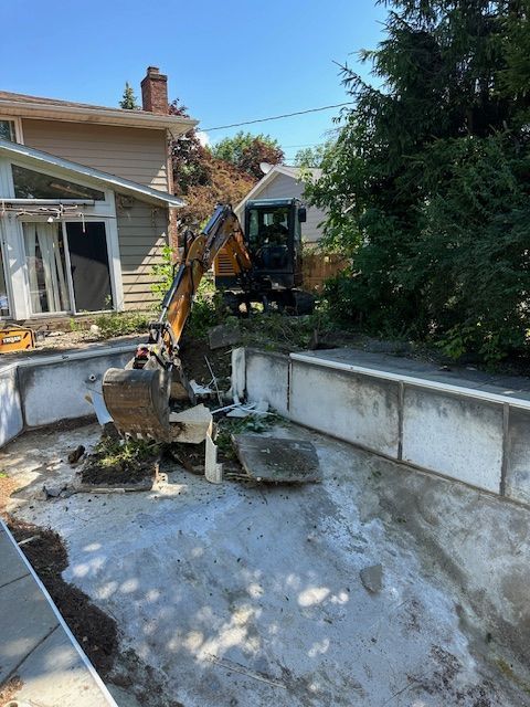 An excavator is working on a swimming pool in front of a house.