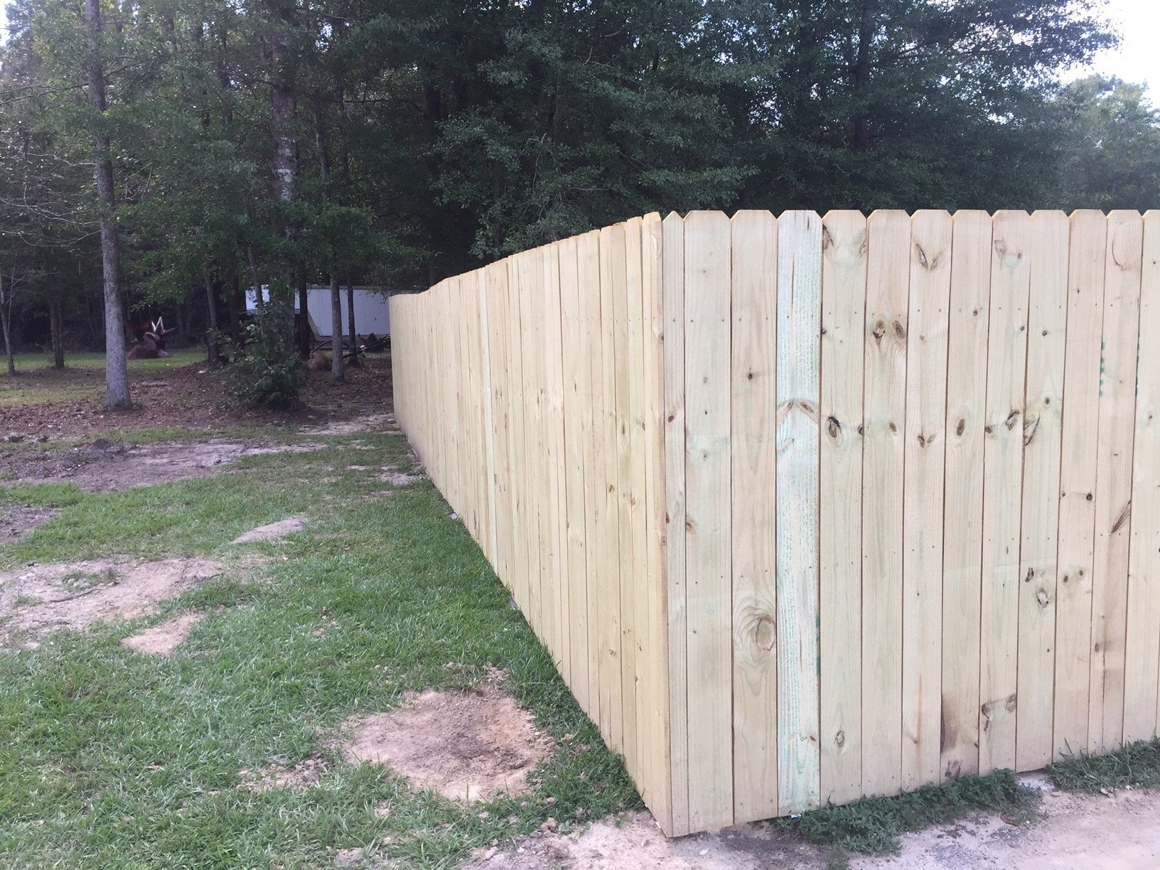New wooden privacy fence beside a grassy yard and trees outdoors