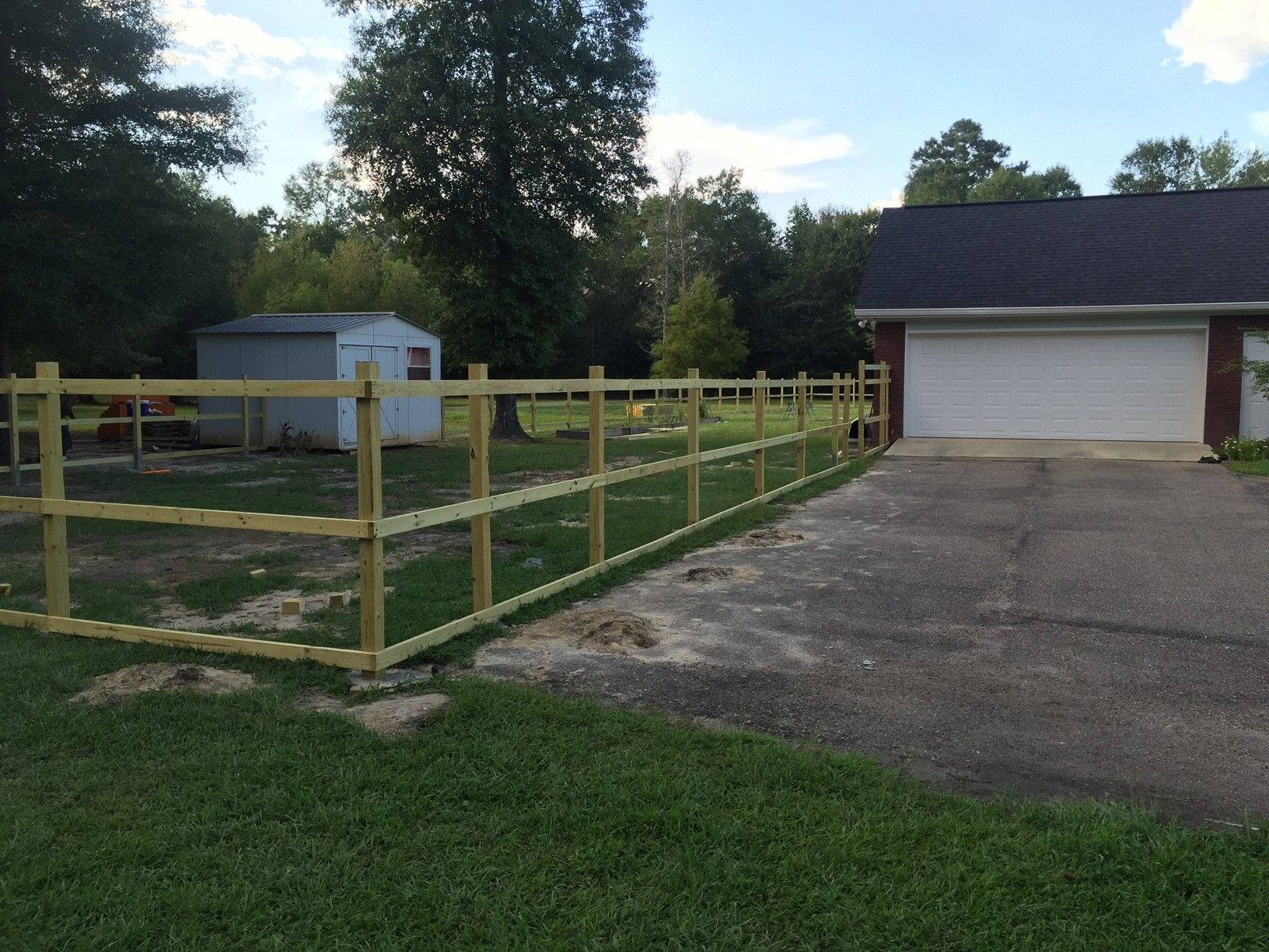 Fenced grassy yard beside a driveway and white garage under a sunny sky