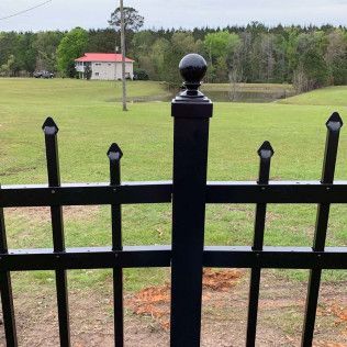 Black metal fence in front of a green field with a small red-roofed house in the distance.