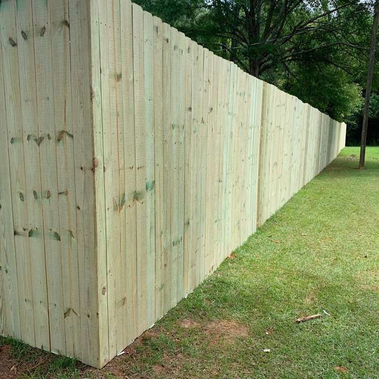 Long wooden privacy fence running along a grassy yard beside trees