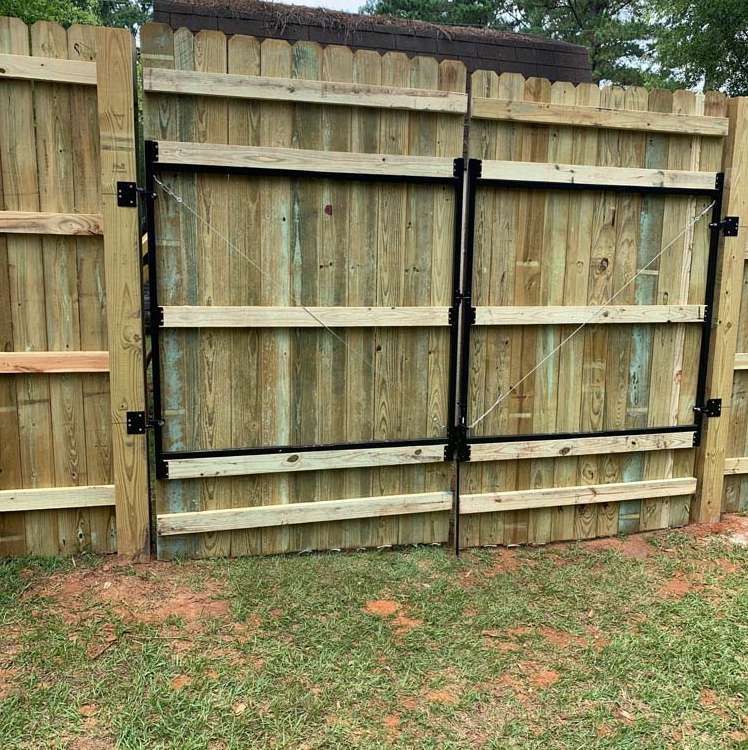 Backyard wooden fence with a repaired double gate and black metal bracing
