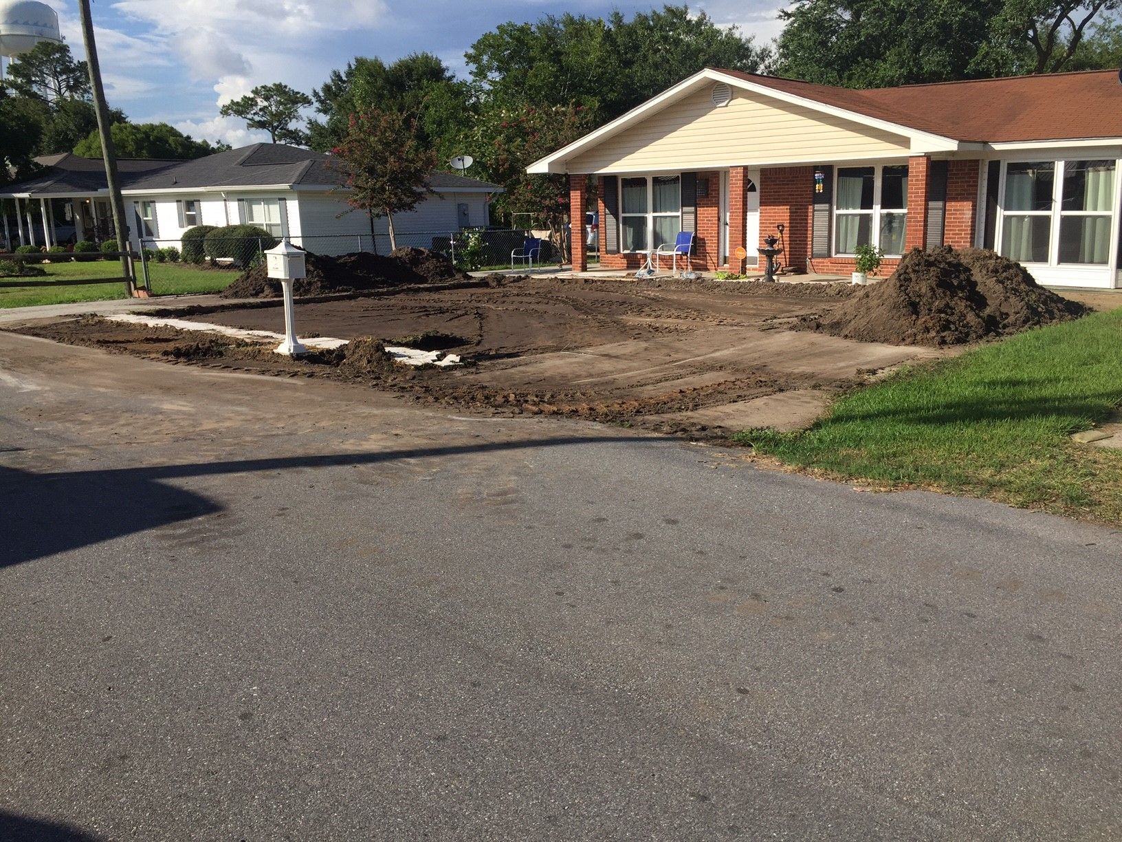 A house under renovation with a torn-up front yard and piles of dirt beside a quiet street.
