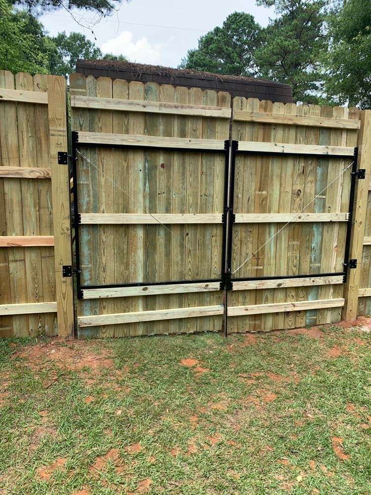 Wooden backyard fence with a double gate and black metal hinges, opening to a grassy yard.