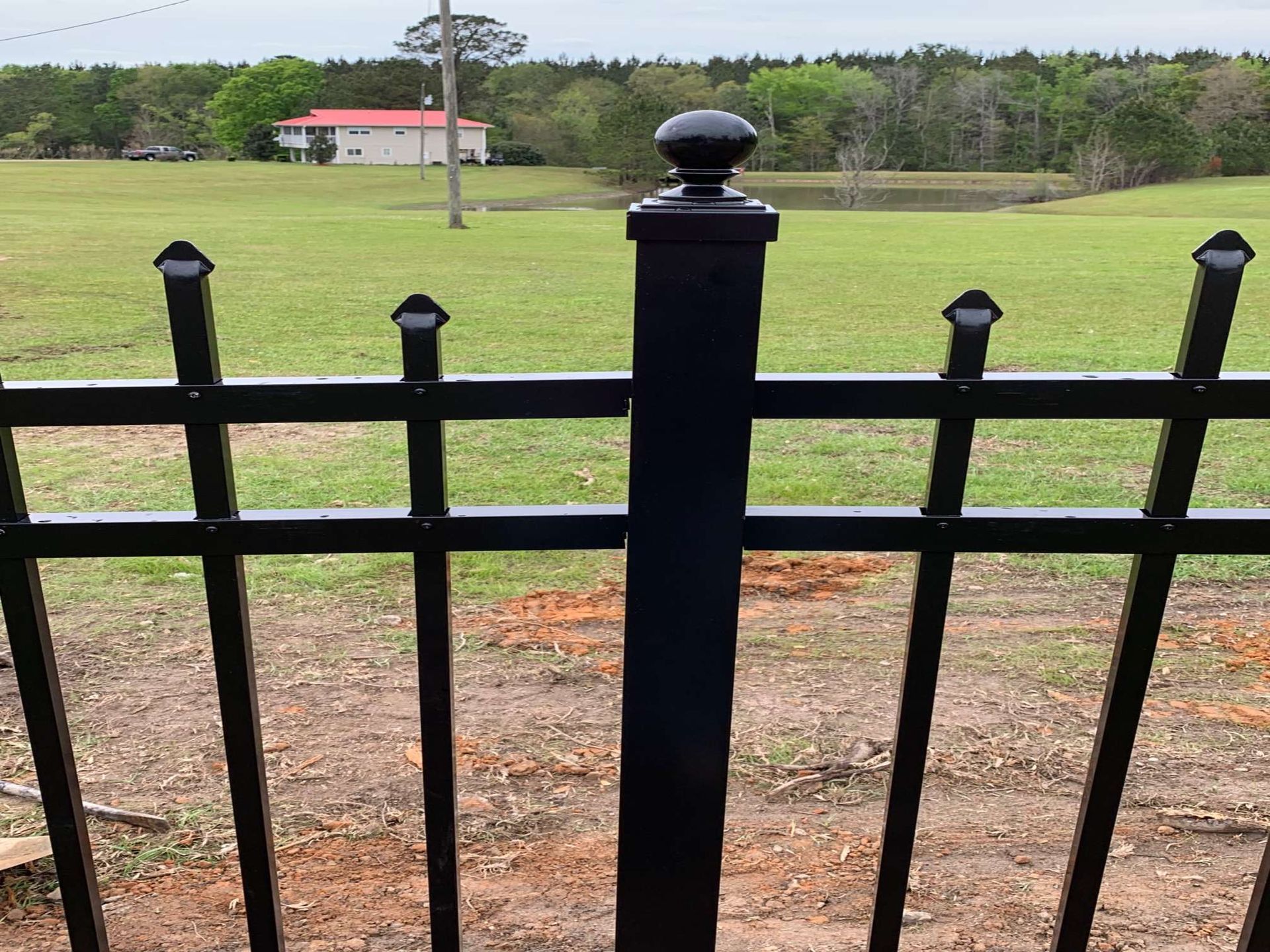 Black metal fence in front of a grassy field with a white building in the distance.