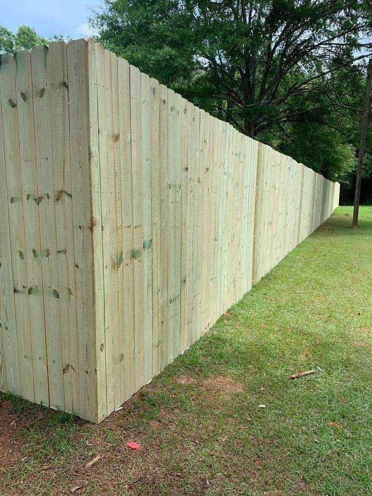 Wooden privacy fence receding along a grassy yard beside trees