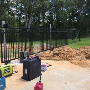 Black metal fence installed beside a dirt pile and construction tools in a wooded yard