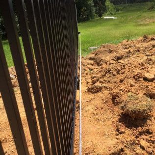 Black metal fence beside a dirt trench and mound in a grassy yard