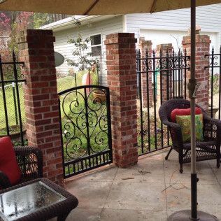 Covered patio with wrought-iron gate, brick pillars, and outdoor chairs beside a yard and house