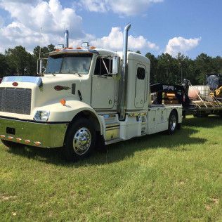 White semi-truck parked on grass towing heavy equipment on a flatbed trailer under a blue sky