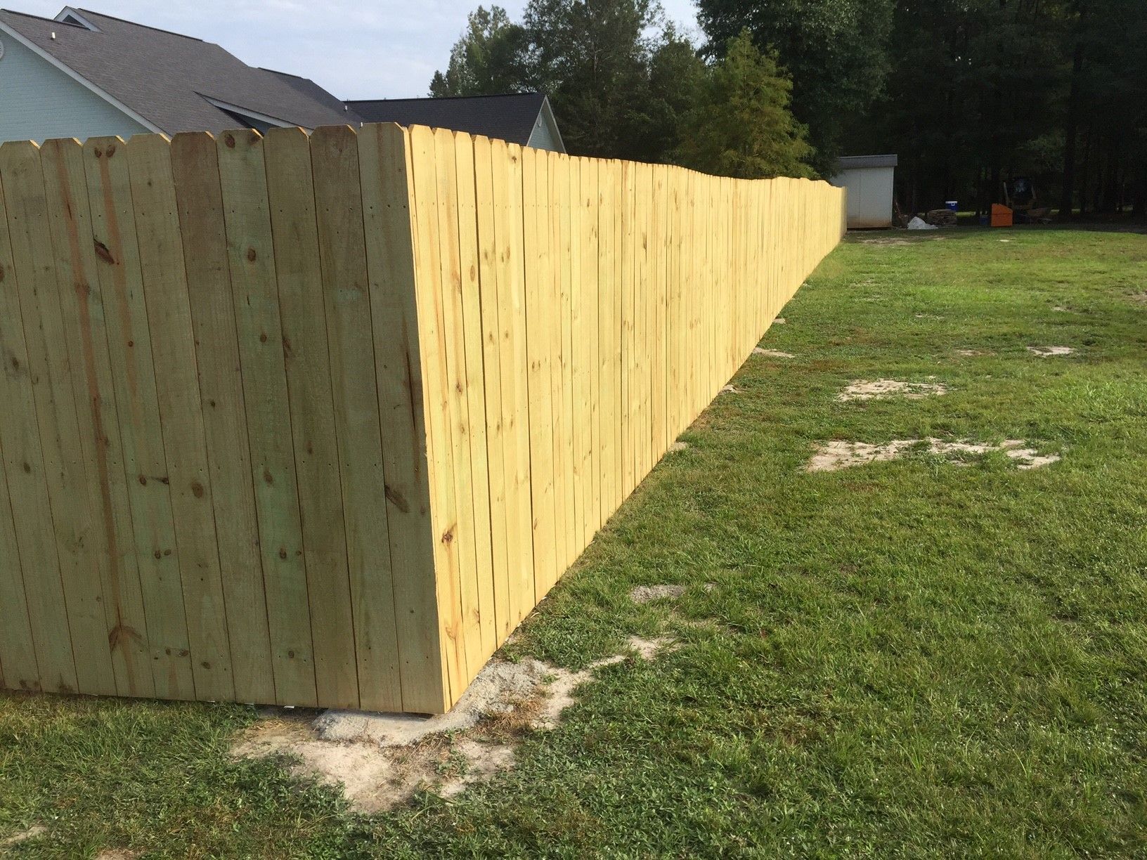 New wooden privacy fence along the edge of a grassy yard near a house