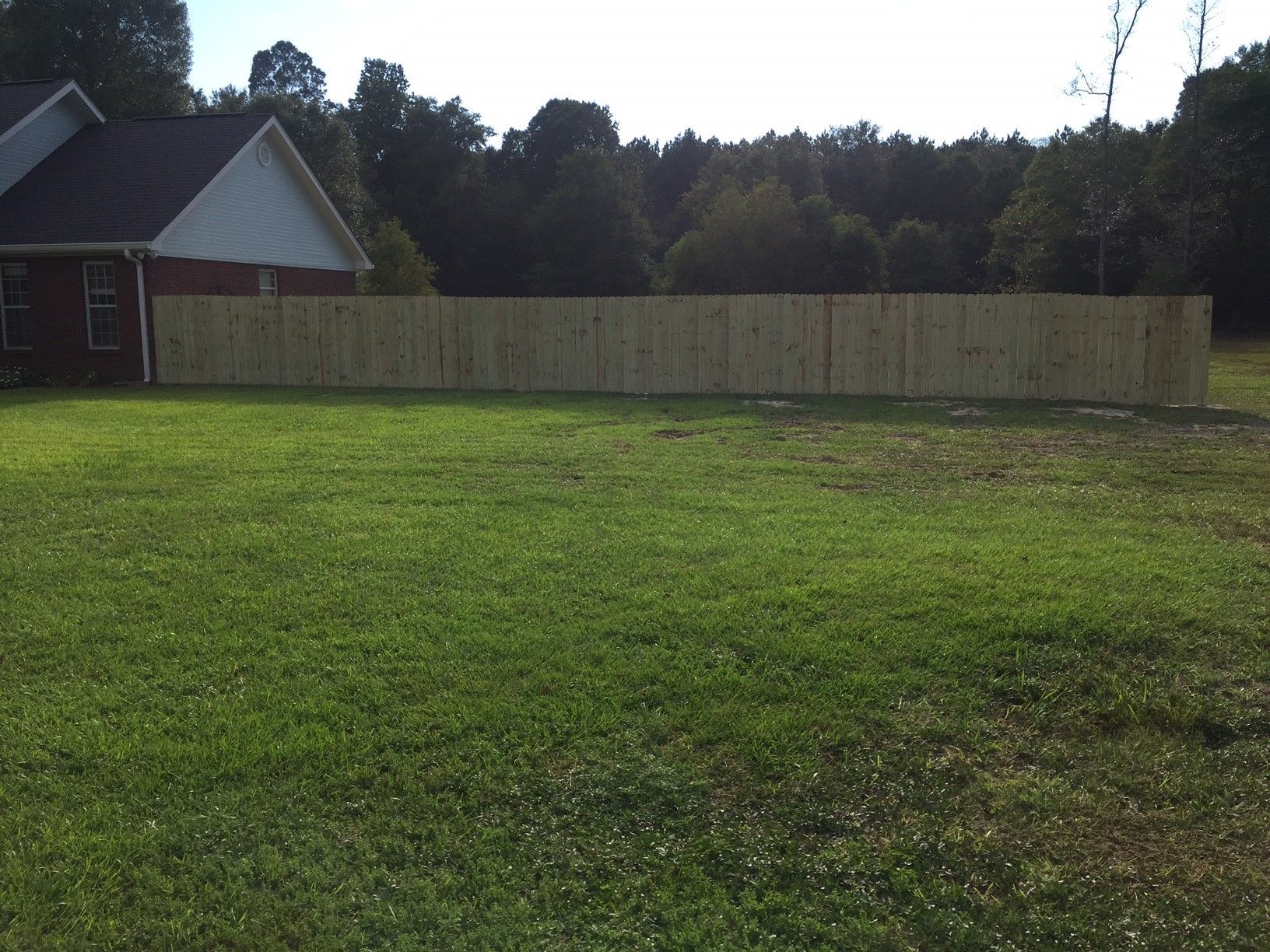 Grassy yard with a long wooden fence, small building on the left, and trees in the background.