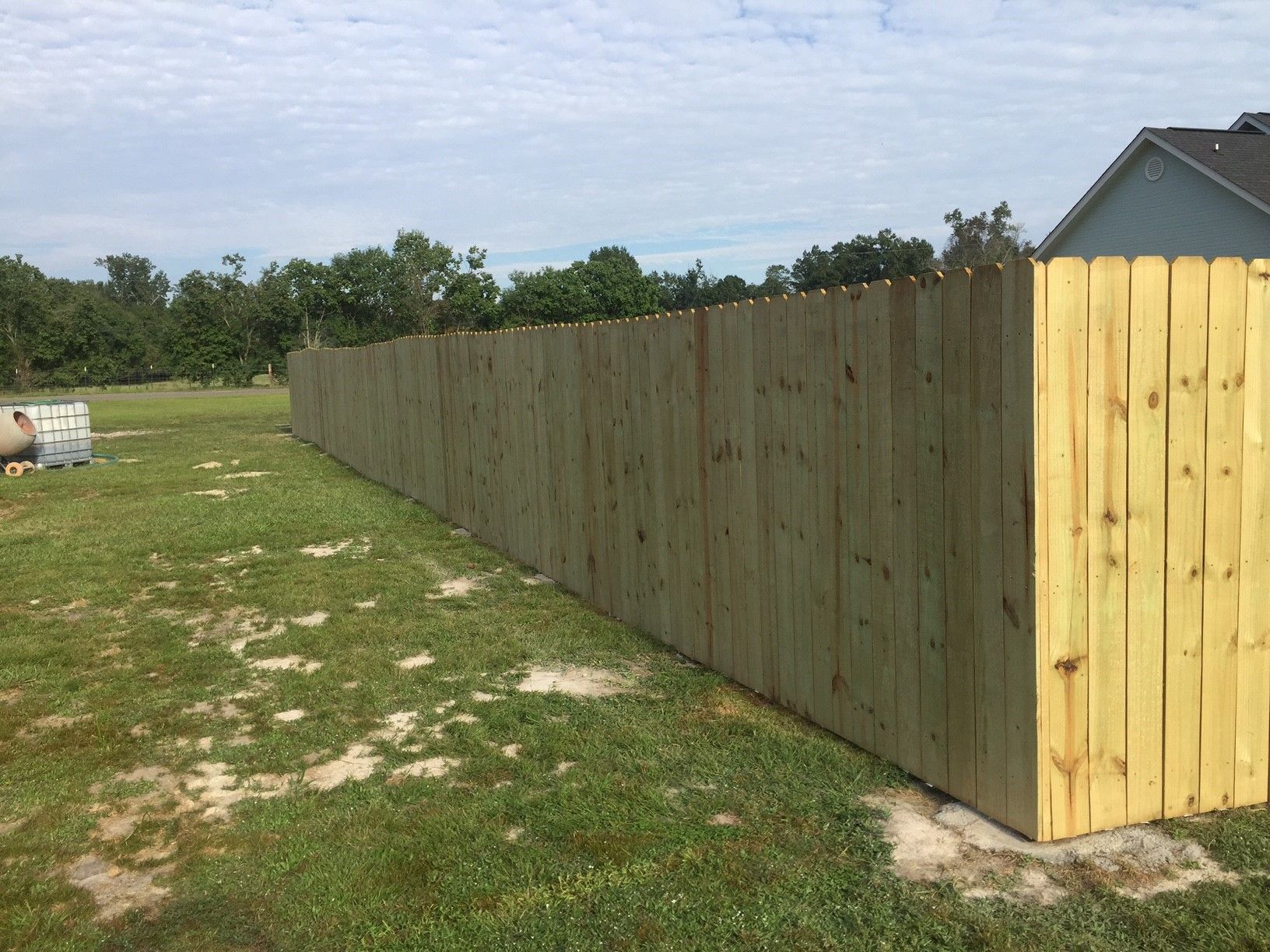Long wooden privacy fence stretching across a grassy yard under a partly cloudy sky.