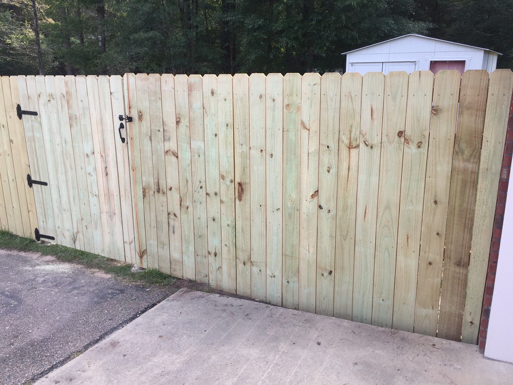 New wooden fence across a driveway, with a white shed visible behind it