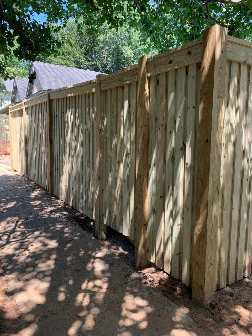 Wooden privacy fence along a shaded dirt path with trees overhead