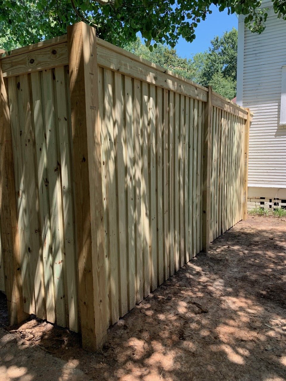 Wooden privacy fence beside a house, with sunlight and tree shadows on the boards.