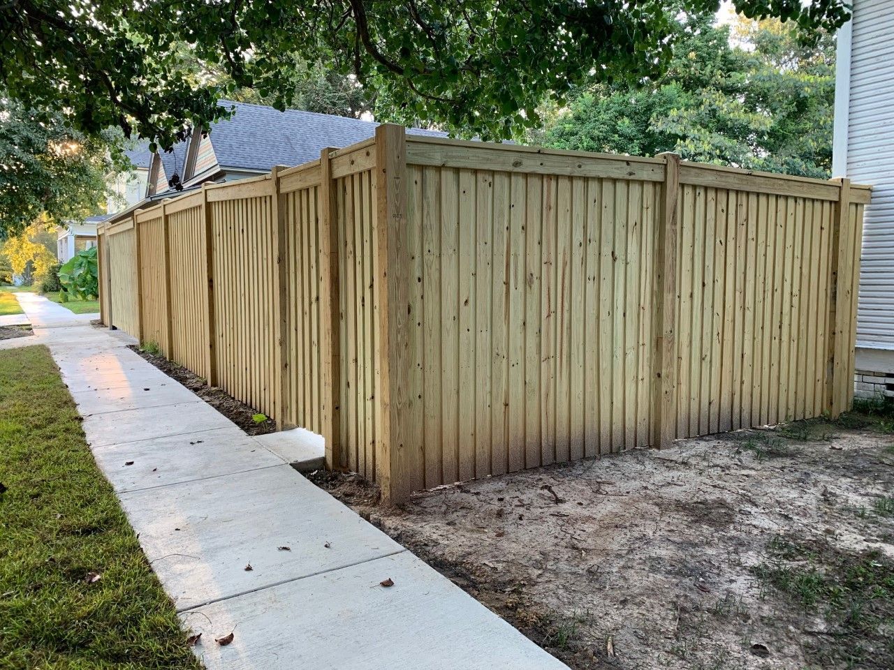Wooden privacy fence along a concrete sidewalk beside a house and grassy yard